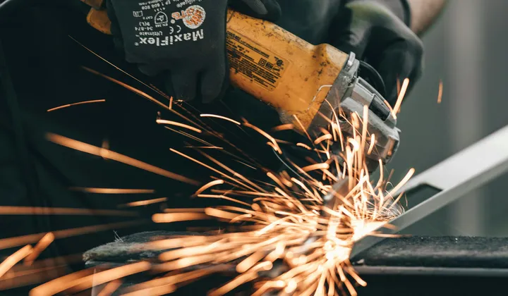 An angle grinder throwing a spray of orange sparks off a steel plate on a bench.